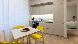 Une cuisine compacte avec des meubles blancs, un évier et un coin repas comprenant une table blanche et des chaises jaunes.