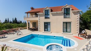 Een huis met twee verdiepingen, een zwembad, een jacuzzi en buiten zitplaatsen.