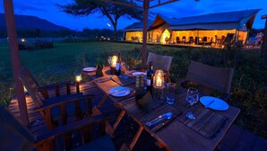 An outdoor dining area with a wooden table set for two, surrounded by chairs, and a canopy overhead. - Asanja Moru (Serengeti)