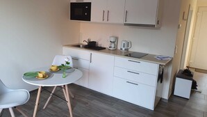 Kompakti keittiö, jossa on mikroaaltouuni, kahvinkeitin ja pieni jääkaappi. Keittiössä on ruokapöytä tuoleineen sekä maljakko, jossa on kukka.