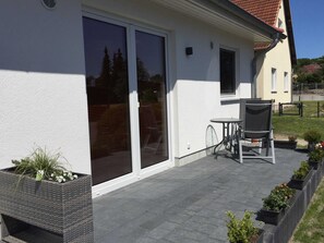 Um pátio com mesa, cadeiras, porta de vidro corria e vasos com plantas.