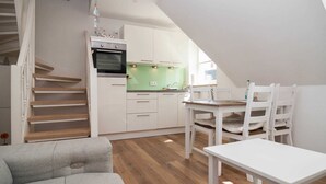 Een kleine keuken met witte kasten, een groene spatwand, en een eethoek met een witte tafel en stoelen.