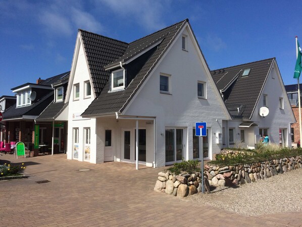 A two-story building with a sloped roof, a visible entrance, and a satellite dish. - Fewo Lütti, Deutschland (Hörnum (Sylt))