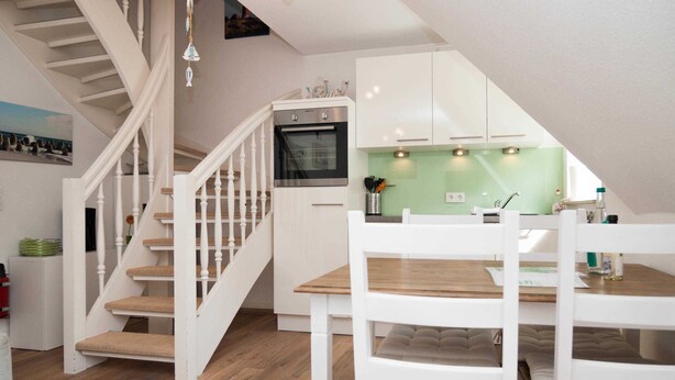 Een moderne keuken met witte kasten, een houten trap en een eethoek met witte stoelen.