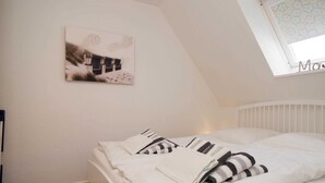 Een net opgemaakt bed met gestreept beddengoed, een wit hoofdbord en een aan de muur bevestigd schilderij.