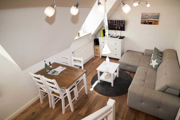 Uma sala de estar aconchegante com uma mesa de jantar de madeira, cadeiras brancas, um sofá cinzento e um tapete preto.