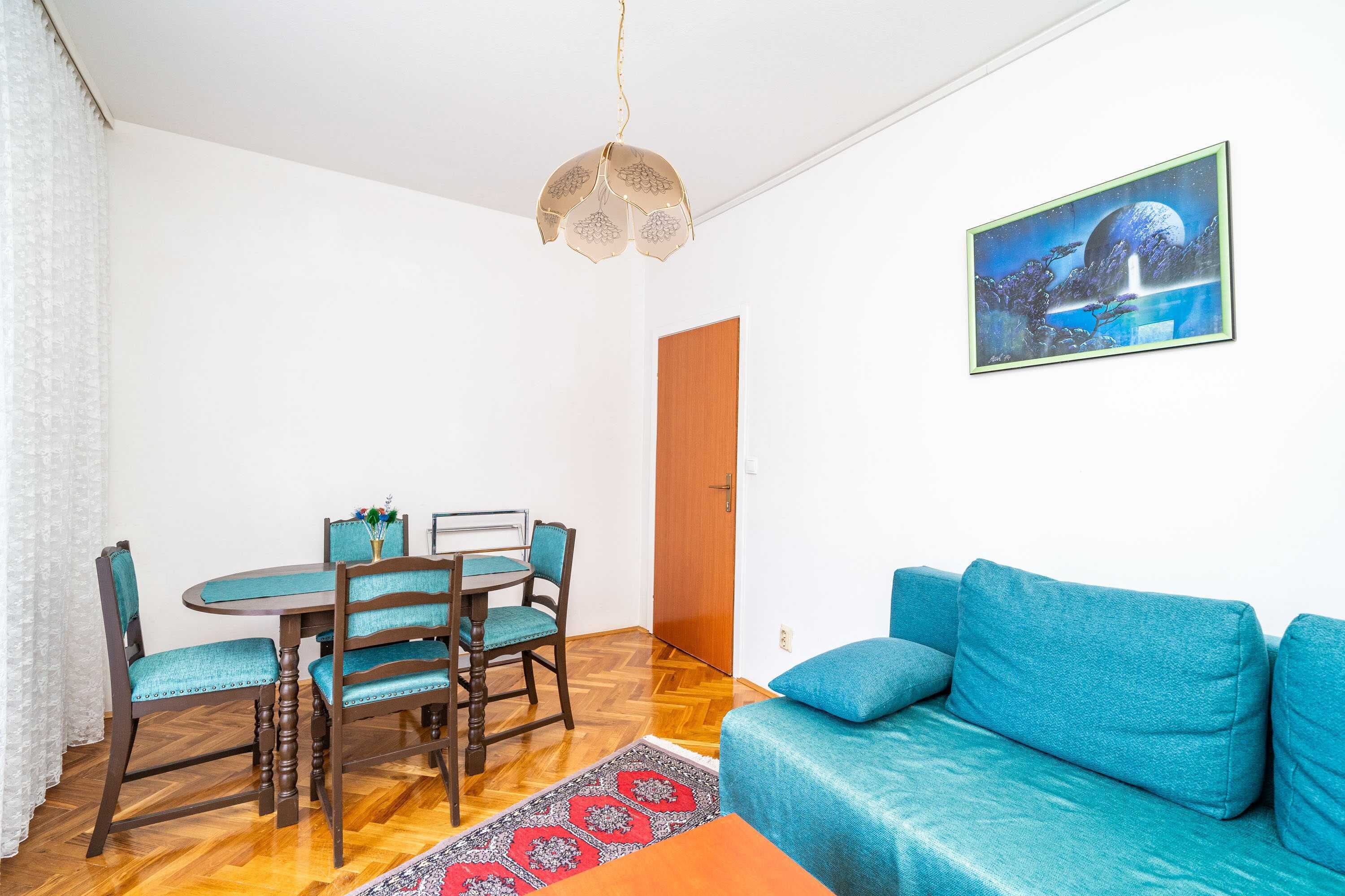 A room with a blue sofa, a dining table with chairs, a hanging light fixture, and a framed picture on the wall.