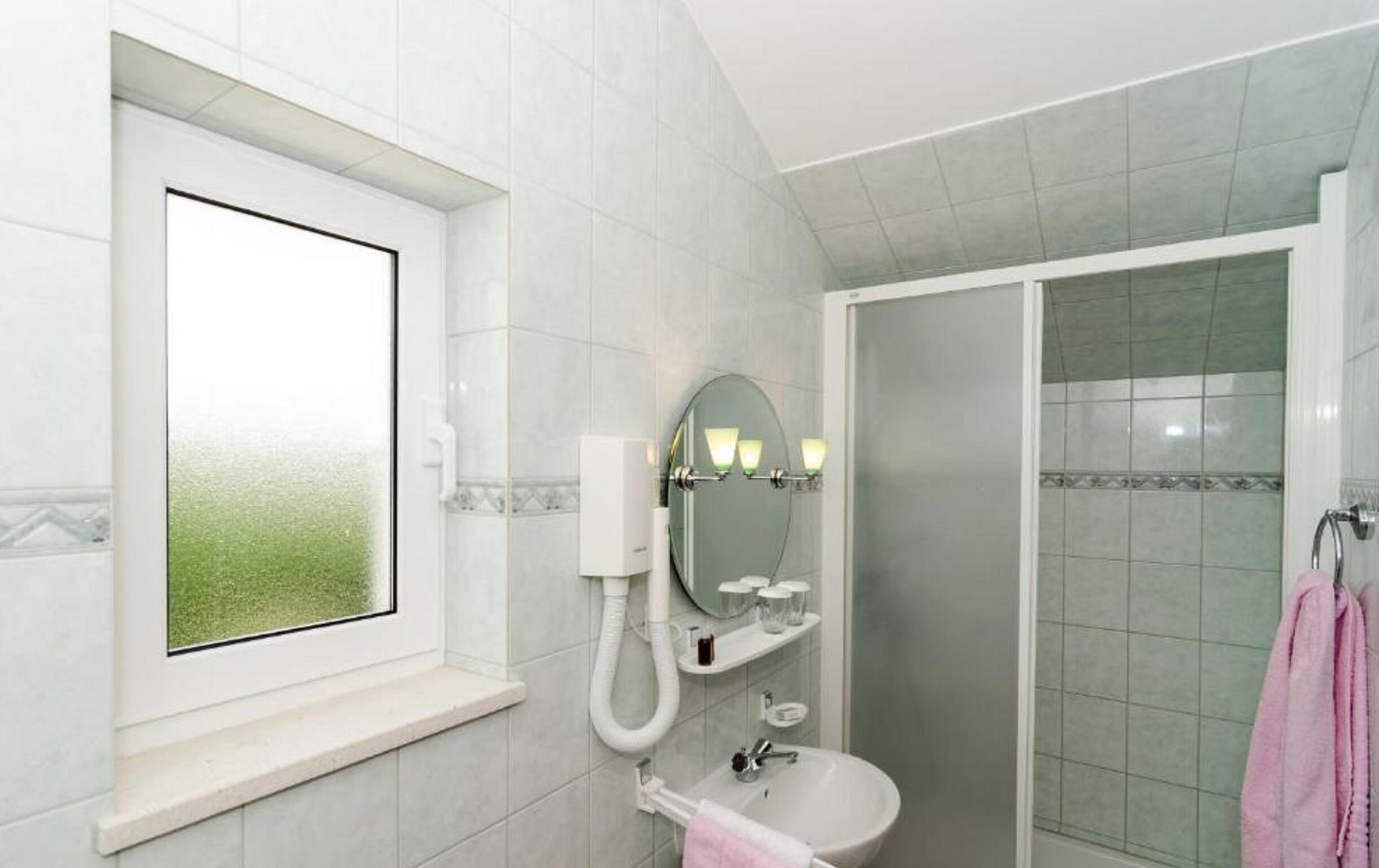 A bathroom with a window, a sink, a mirror, and a shower.