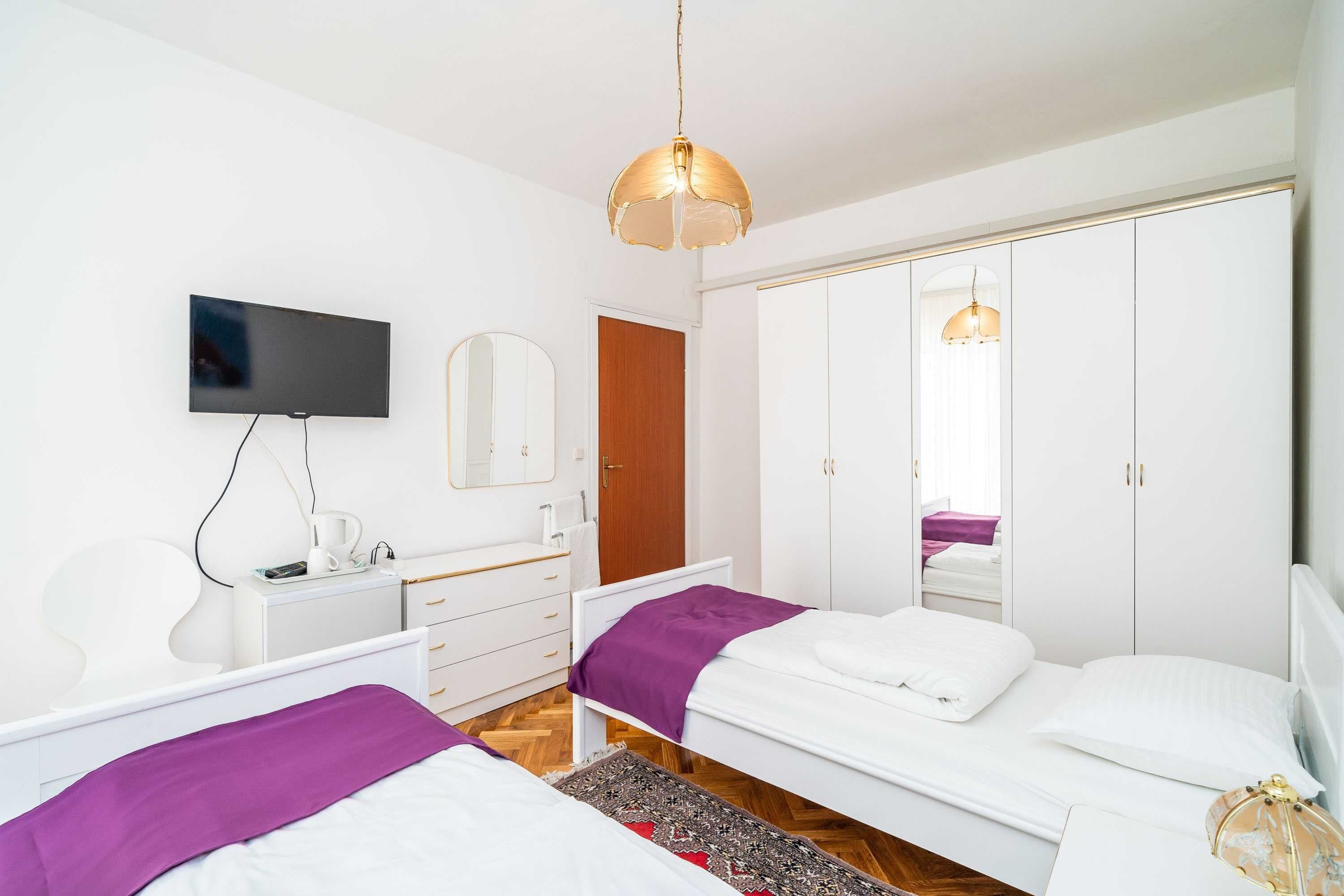 A modern bedroom with two beds, a TV, a wardrobe, and a mirror.