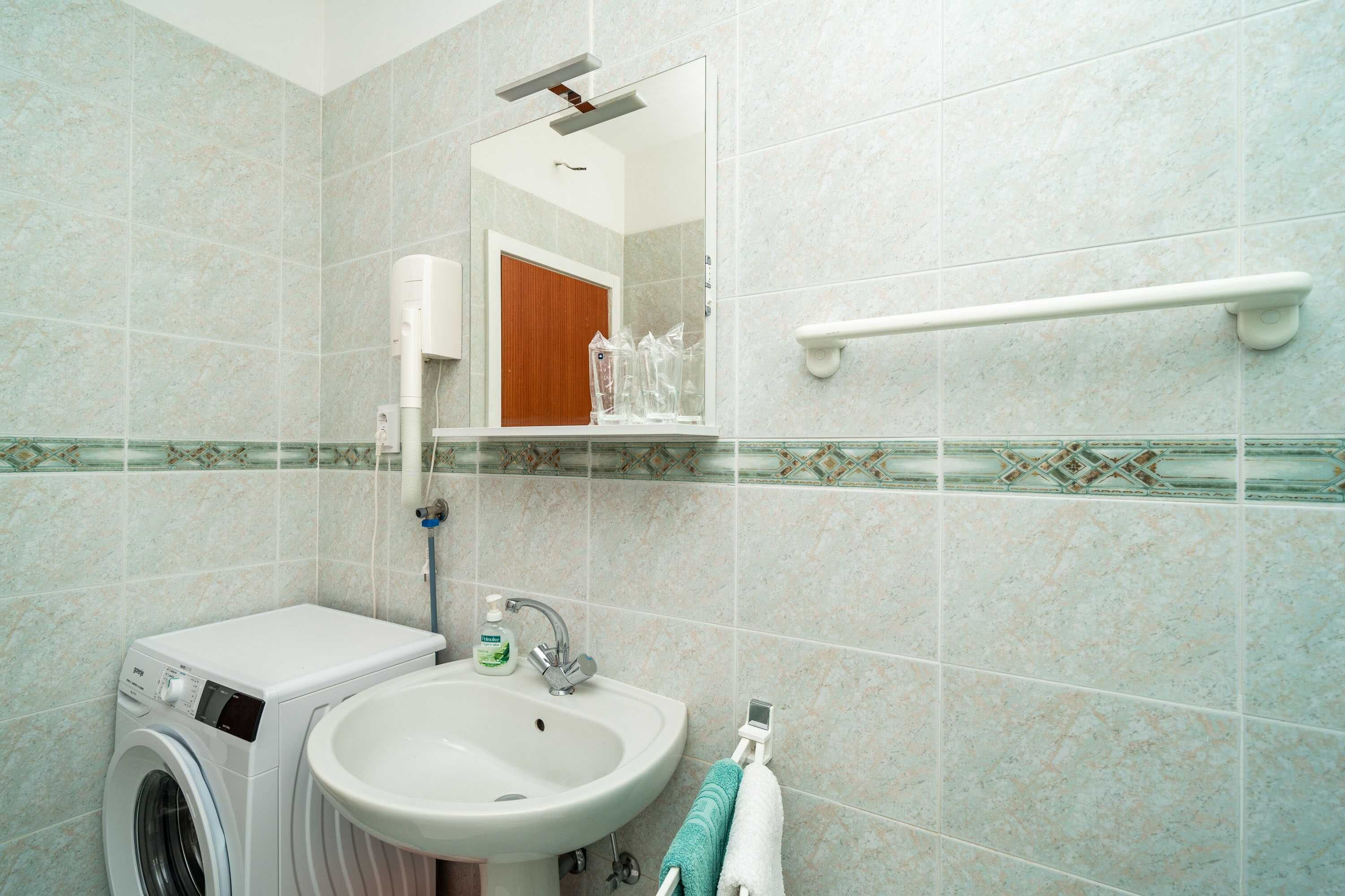 A bathroom with a washing machine, sink, and a mirror.