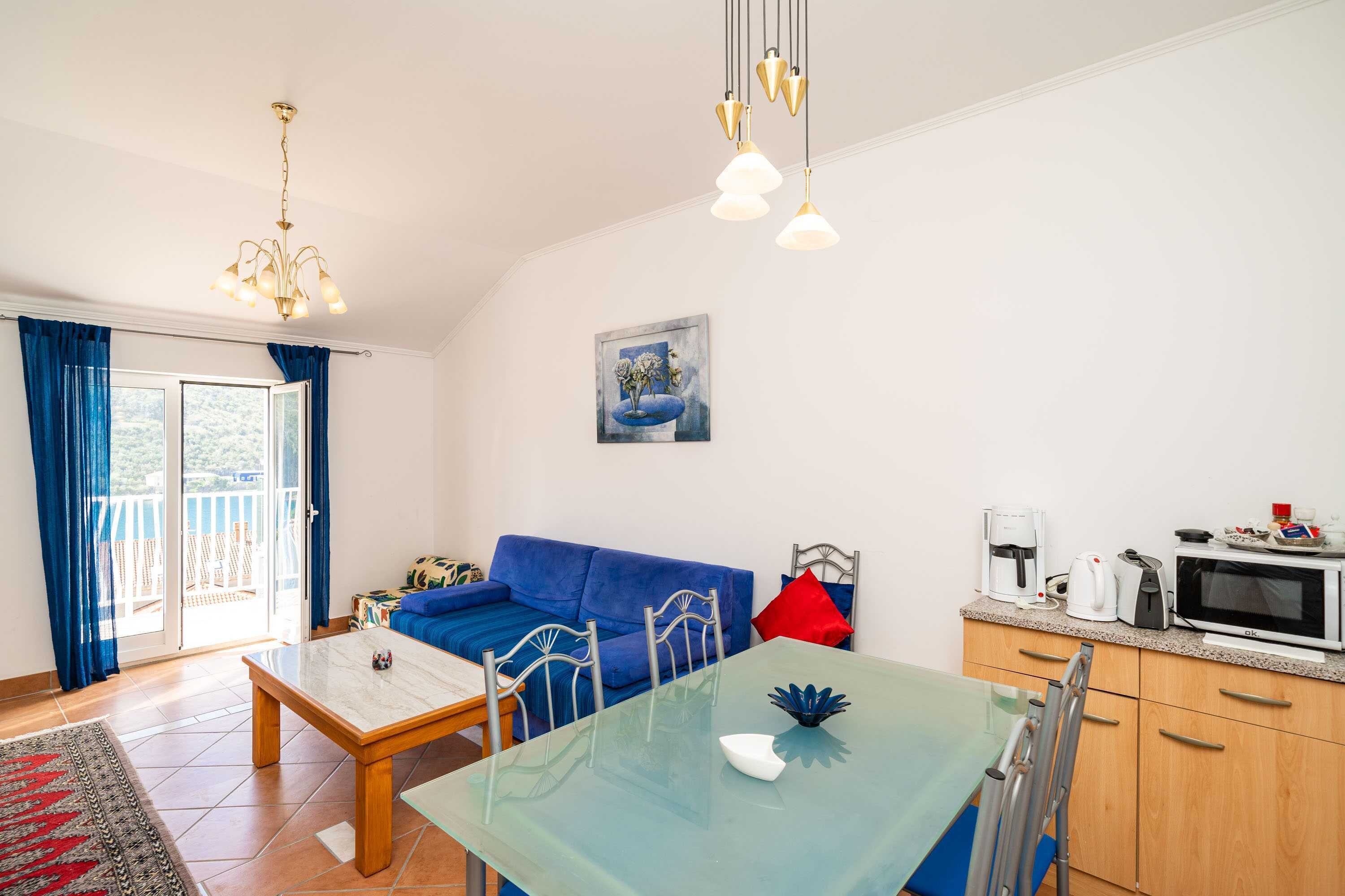 A living room with a blue sofa, a dining table, and a kitchen area with a microwave.