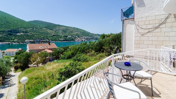 En balkon med et bord og stole, der kigger ud over et kystområde med huse og et bjerg.