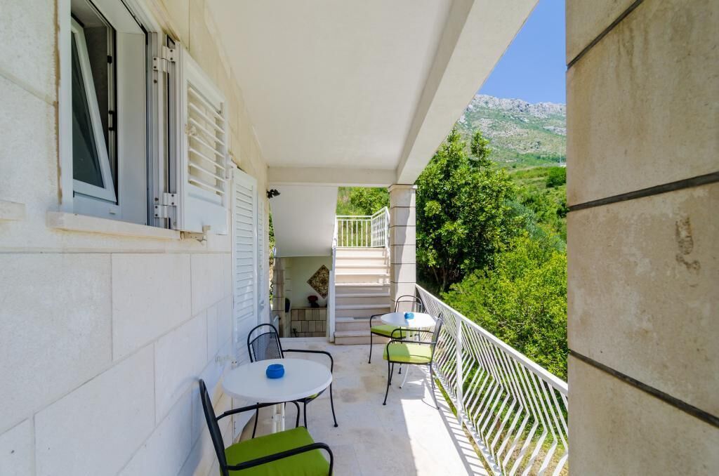 A balcony with a table and chairs, a staircase, and a view of greenery and mountains.