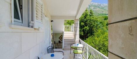 A balcony with a table and chairs, a staircase, and a view of greenery and mountains.