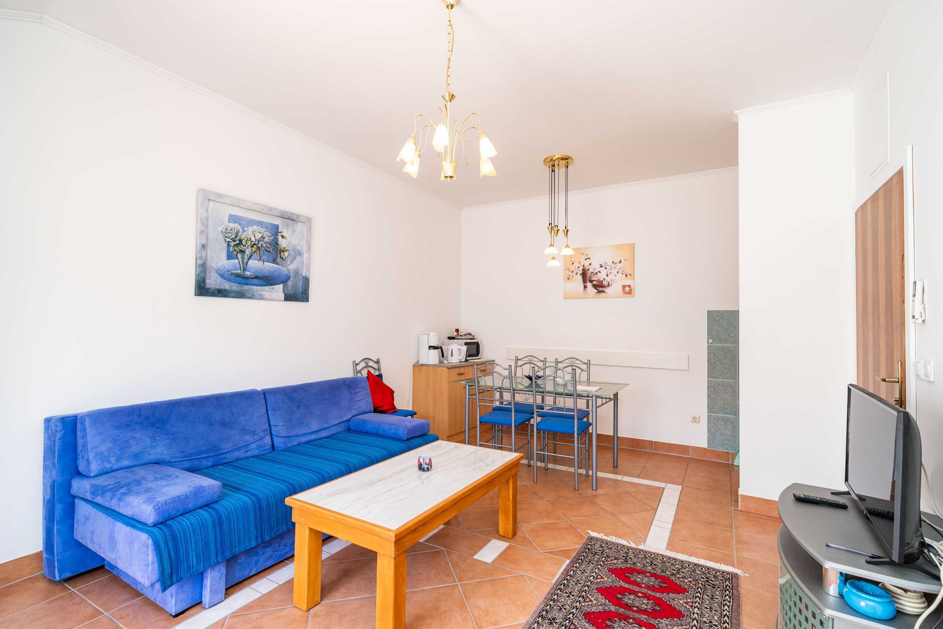 A living room with a blue sofa, a wooden coffee table, a TV, and a dining area with chairs and a table.