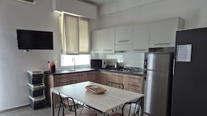Eine moderne Küche mit Esstisch, Stühlen, einem Kühlschrank und einem an der Wand befestigten Flachbildfernseher.