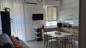 Ein modernes Wohnzimmer mit einer Couch, einem Esstisch und Stühlen. Es gibt eine Küchenzeile mit Schränken und einer Mikrowelle.