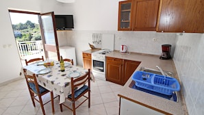 A compact kitchen with wooden cabinets, a gas stove, a coffee maker, and a dining area with a table and chairs. - Apartment Classic Korčula  (Korcula)
