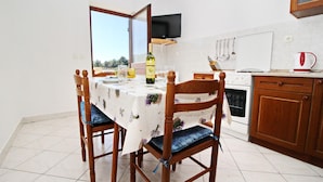 A dining area with a table set for four, a bottle of wine, and a view through an open window. - Apartment Classic Korčula  (Korcula)