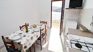 A small dining area with a table set for two, a stove, and a television mounted on the wall. - Apartment Classic Korčula  (Korcula)
