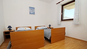 A bedroom with two wooden beds, a nightstand with a lamp, a small table, and a window with curtains. - Apartment Classic Korčula  (Korcula)