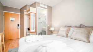 A hotel room with a bed, a bathroom, a door, and a chair. - Hotelli Jokipuisto (Kotka)