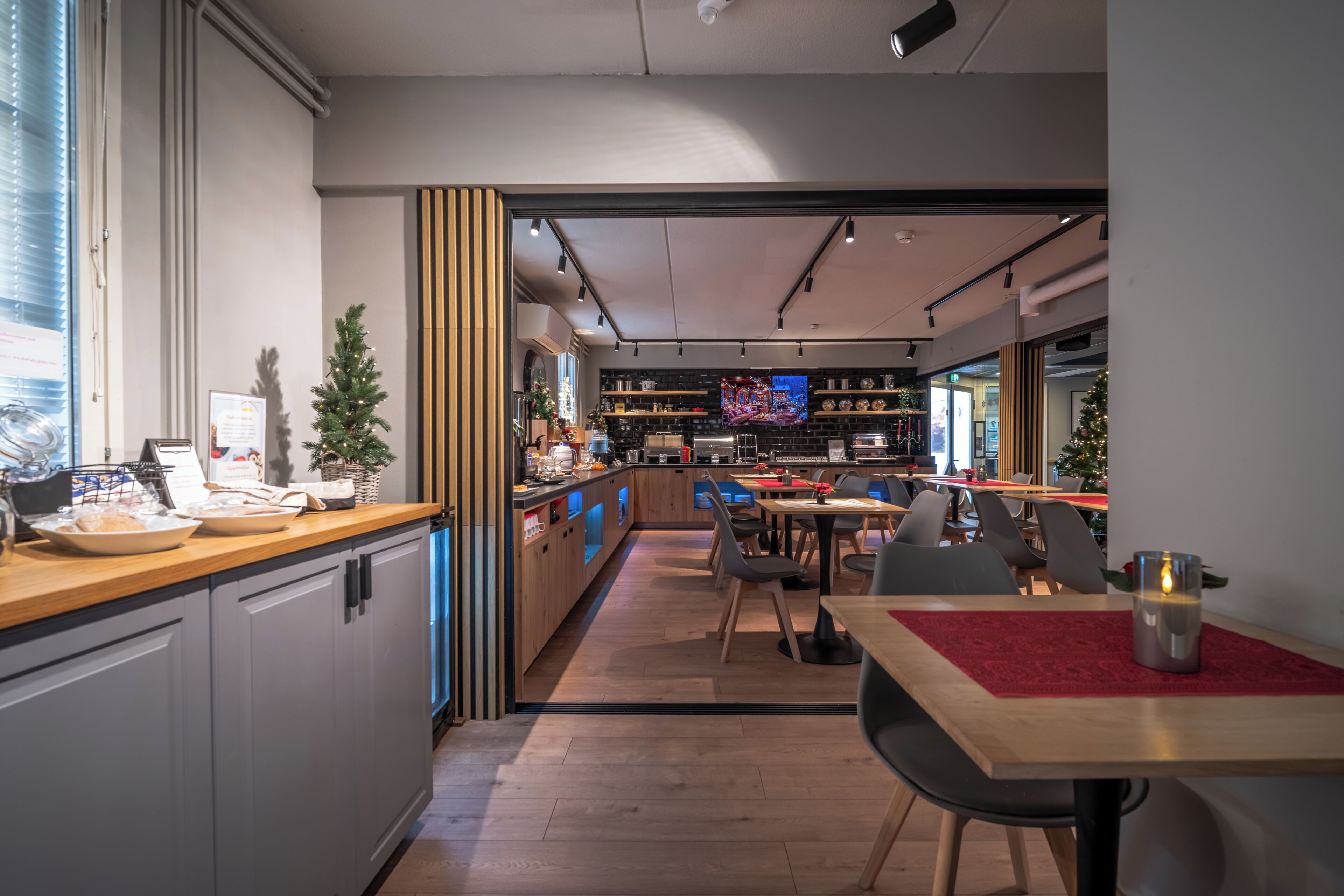Une cuisine moderne avec un plan de travail en bois, un coin repas agrémenté d’un chemin de table rouge et un téléviseur en arrière-plan.