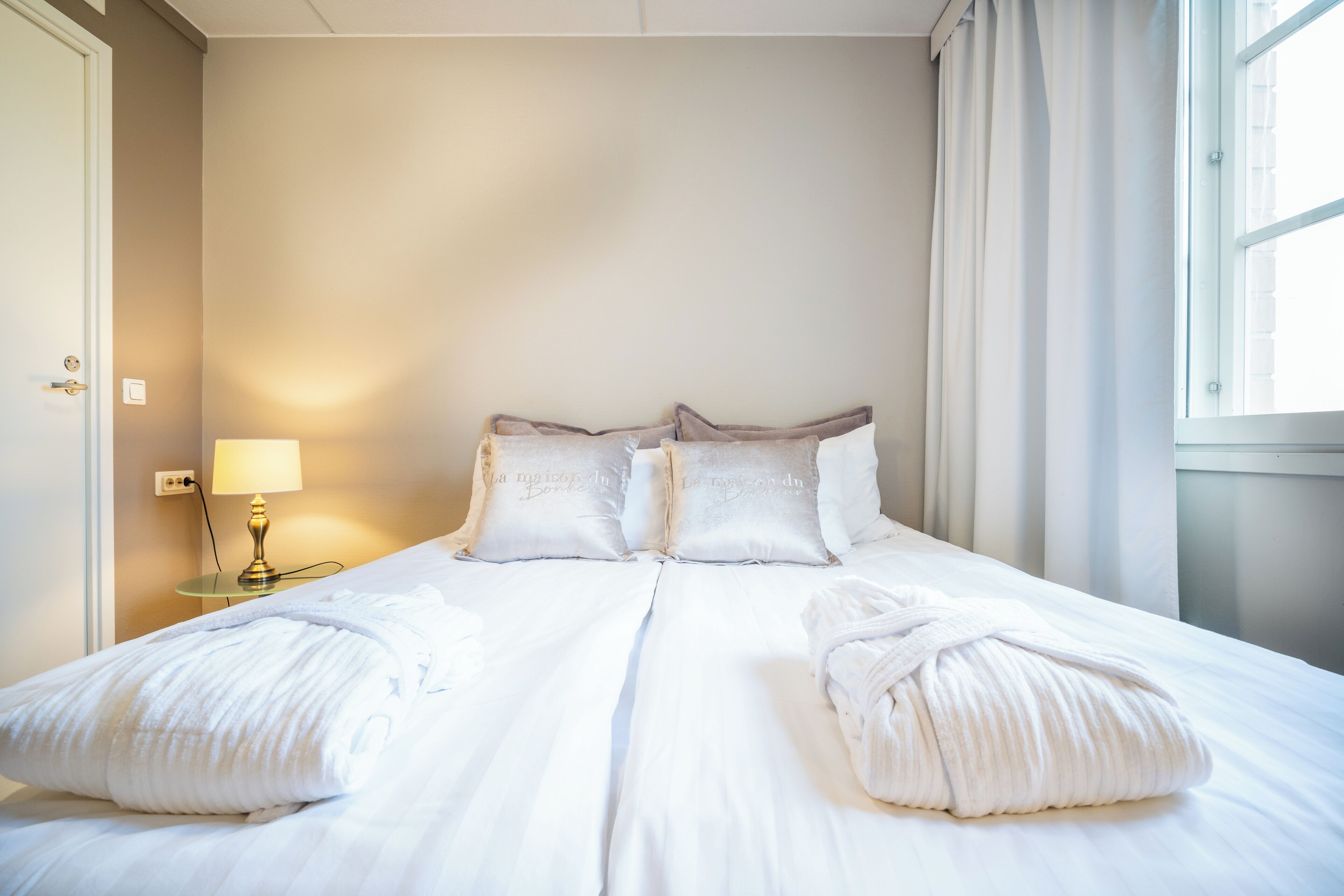 A hotel room with a large bed, two bedside lamps, and a window with curtains.