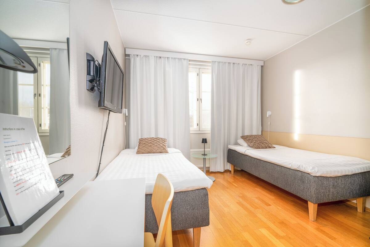 A hotel room with a desk, two beds, a TV, and a window with curtains.