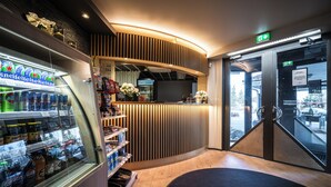 A hotel reception area with a refrigerated display case, a wooden reception desk, and a black mat in the center. - Hotelli Jokipuisto (Kotka)