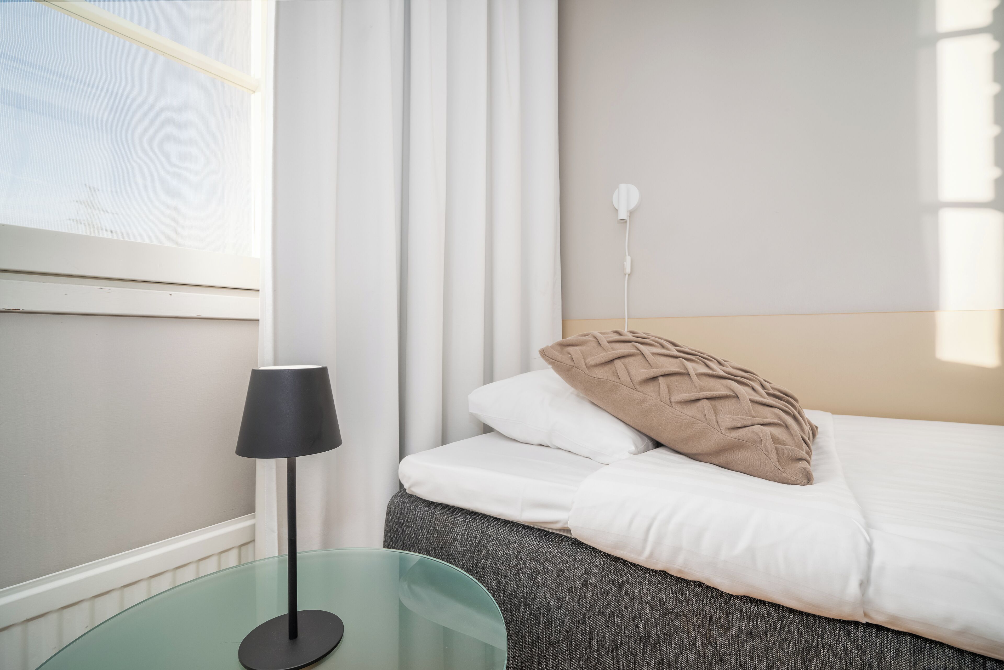 A neatly arranged bedroom with a bed, a bedside table with a lamp, and a power outlet on the wall.