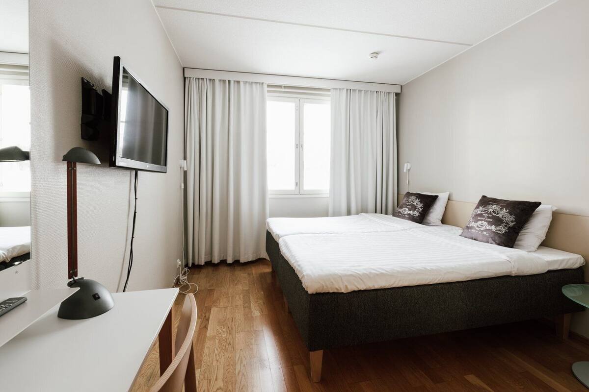 A modern bedroom with a bed, a desk, a TV, and a window with curtains.