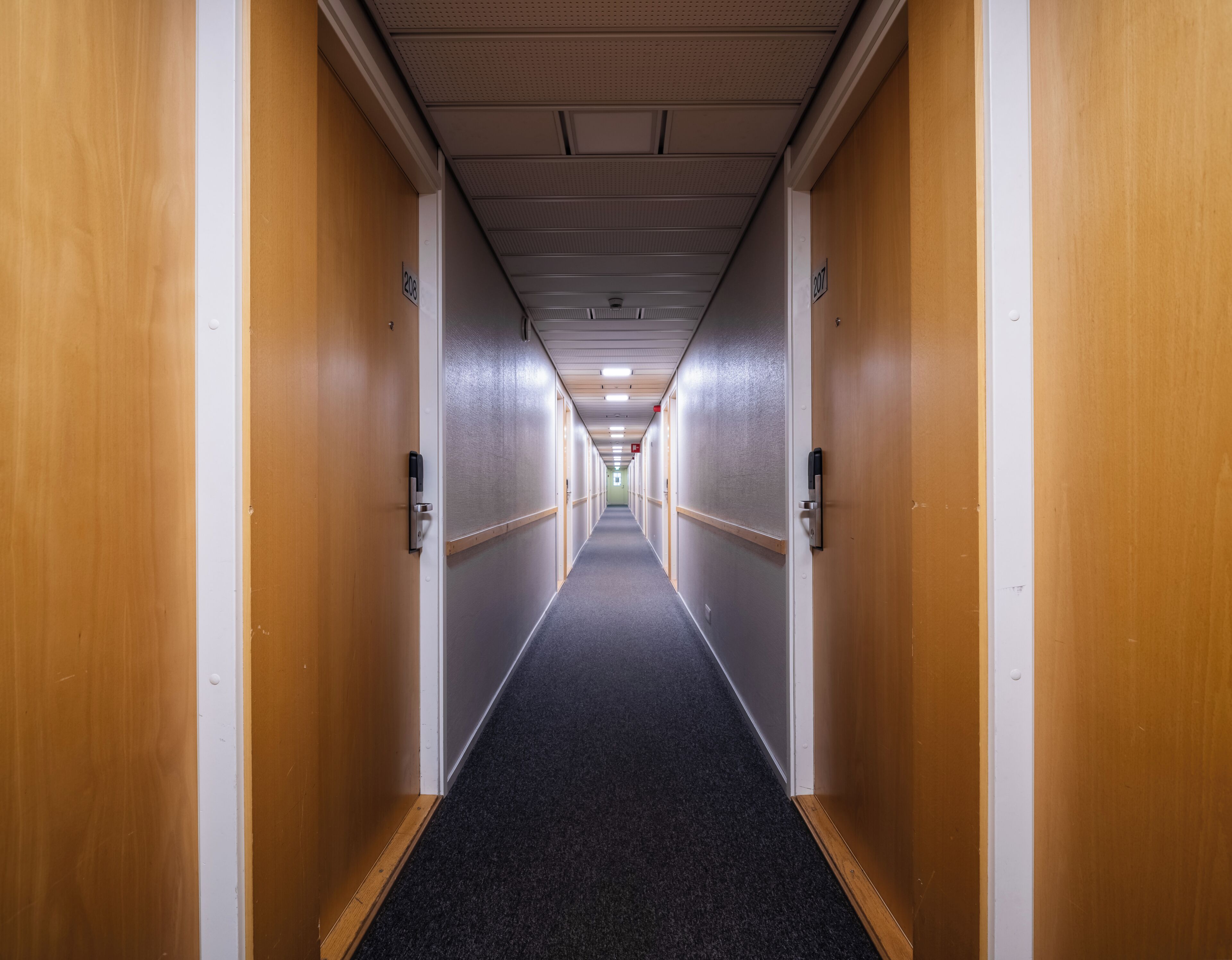 Een lange, smalle gang met houten deuren aan beide kanten, die naar afzonderlijke kamers leidt.