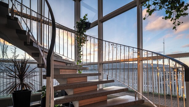 A modern staircase with a glass railing, leading to a high floor with a view of a body of water. - Hotelli Jokipuisto (Kotka)