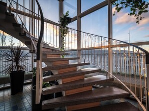 A modern staircase with a glass railing, leading to a high floor with a view of a body of water.