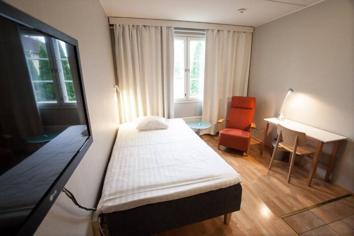 A hotel room with a bed, a TV, a desk, a chair, and a window with curtains.