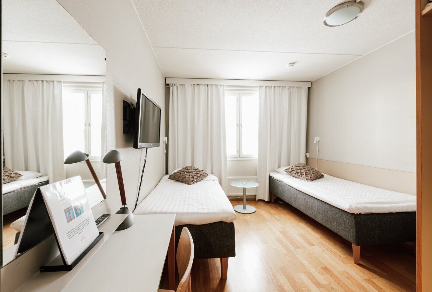Een hotelkamer met twee eenpersoonsbedden, een bureau met een laptop, een aan de muur bevestigde televisie en een klein tafeltje.