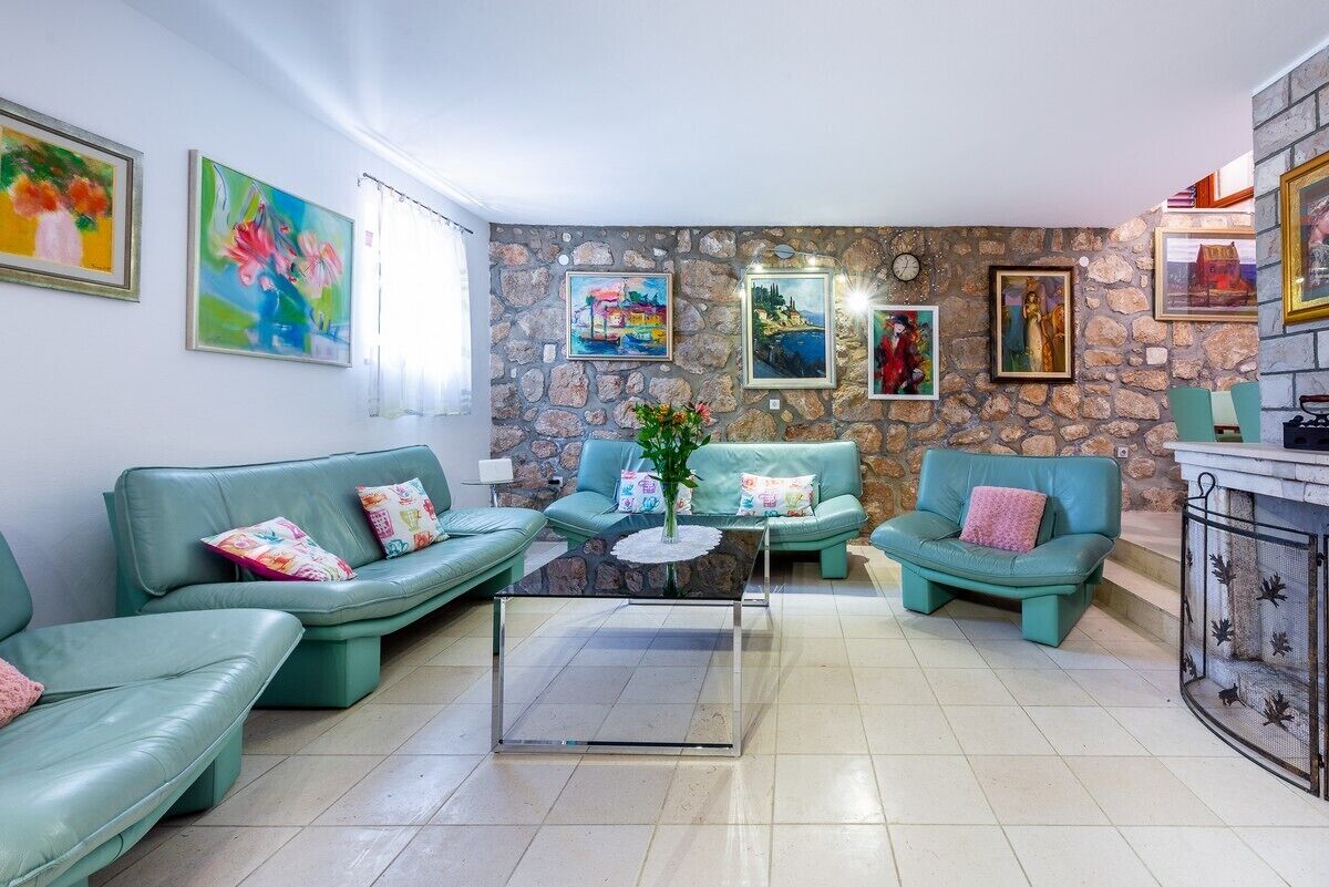 A living room with teal sofas, a glass coffee table, and a stone wall with framed artwork.