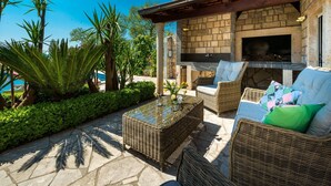 An outdoor patio with wicker furniture, a stone table, and a brick oven. - Villa Mia - Trsteno (Dubrovnik)
