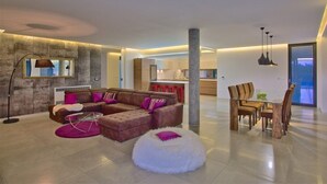 A modern living room with a sectional sofa, a glass dining table, and a white pouf.