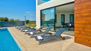 A modern outdoor pool area with lounge chairs and a pool table.