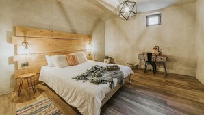 A bedroom with a wooden headboard, a bed with pillows, a bedside table, a desk with a chair, and a small window.