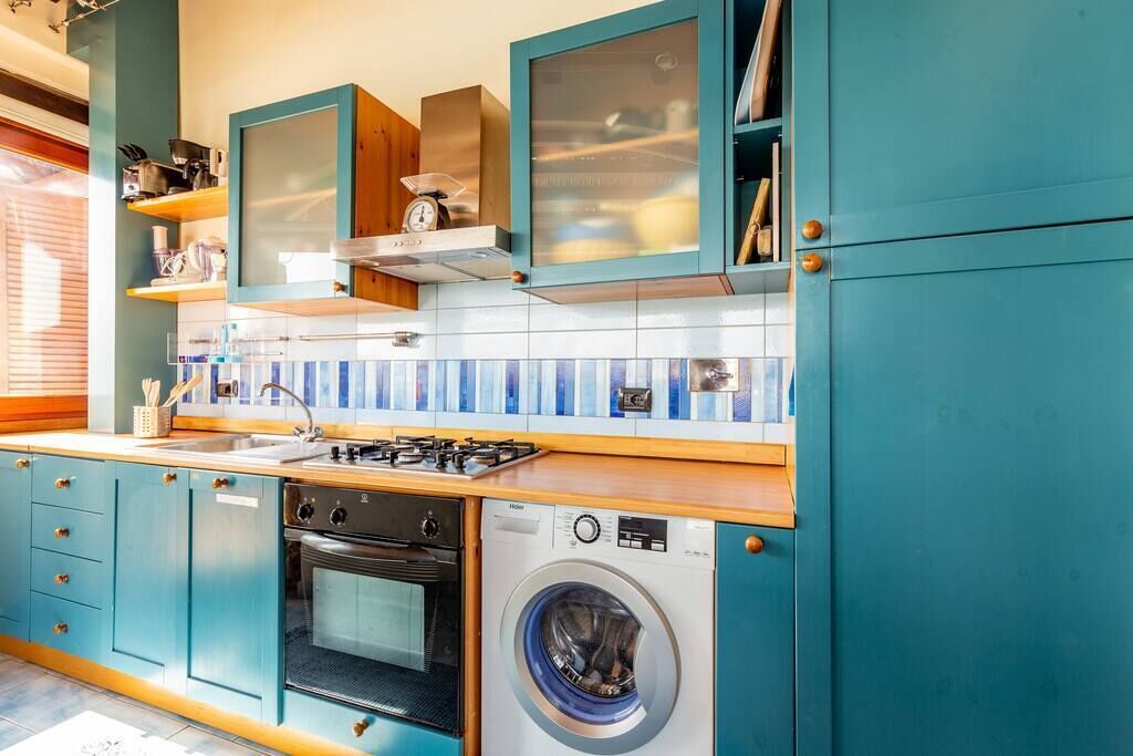 Une cuisine compacte avec des meubles de couleur turquoise, une cuisinière à gaz, un four et un lave-linge à chargement frontal.