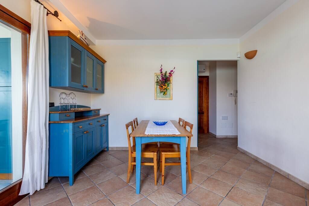 Une cuisine de taille réduite avec des meubles bleus, une table à manger avec quatre chaises et un petit tableau décoratif accroché au mur.
