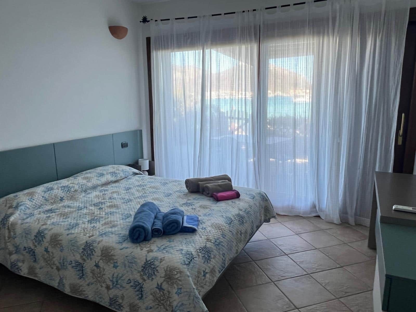Ein Hotelzimmer mit Bett, Schreibtisch und Blick durch transparente Vorhänge.