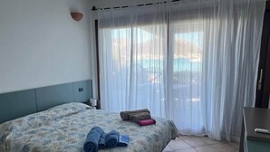 Hotellihuone, jossa on sänky, työpöytä ja näkymä ohuiden verhojen läpi.