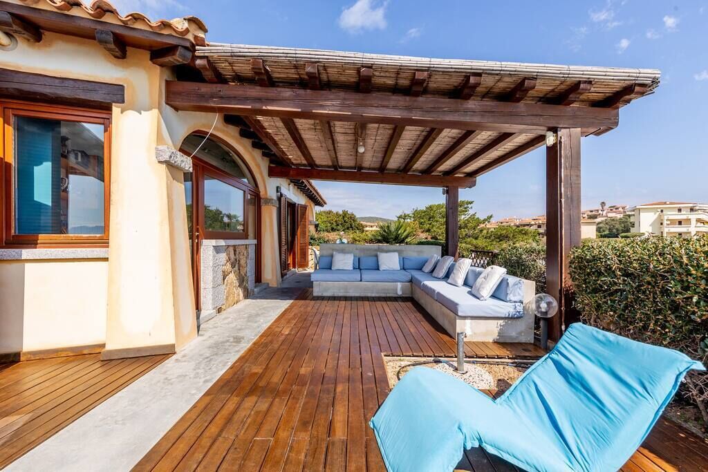 Zona relax esterna coperta con pavimento in legno, un divano e una poltrona da lounge.