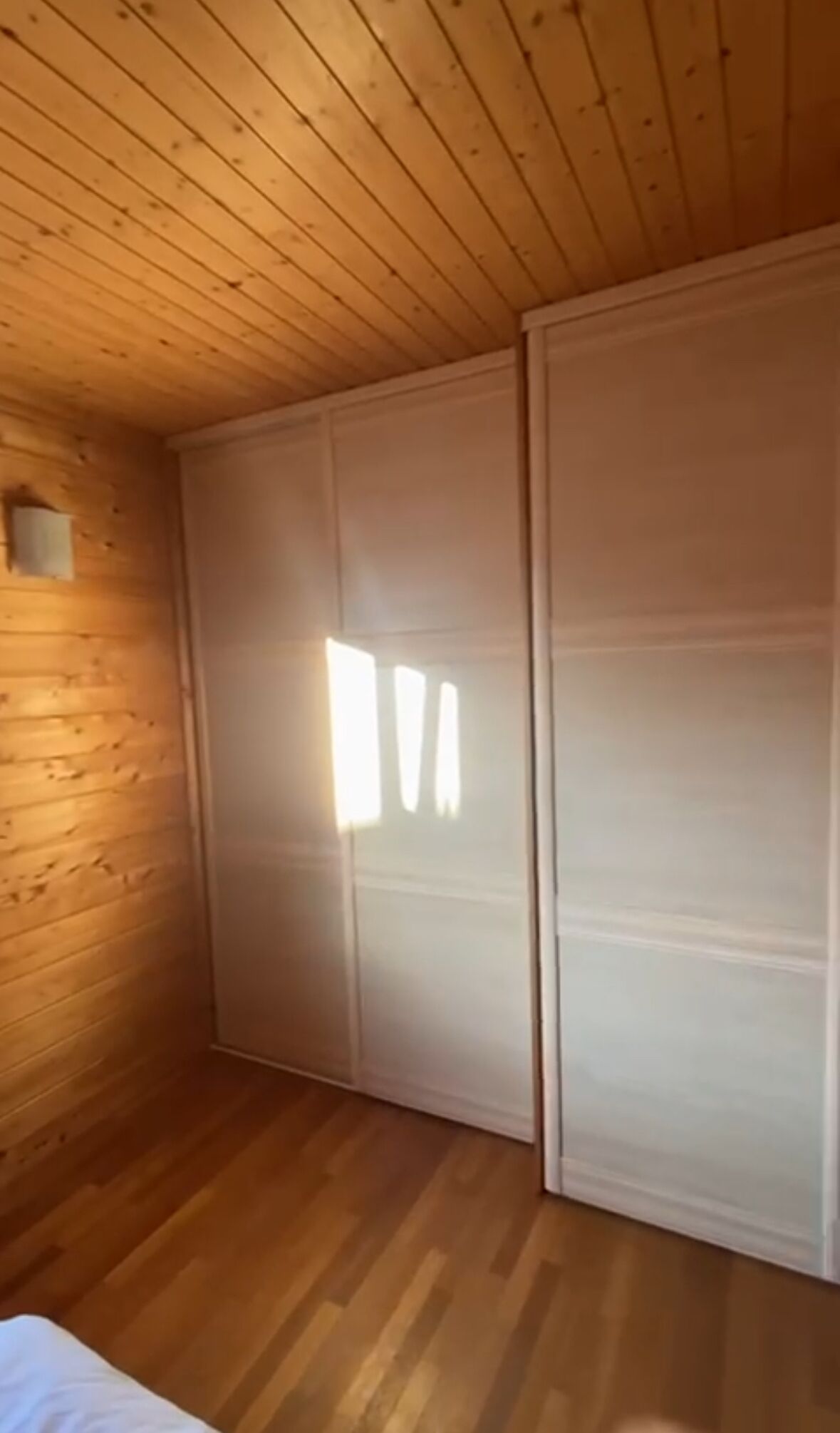 Een kamer met houten wanden en een schuine kap, met een grote schuifdeur en een klein raam.