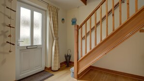 Una escalera de madera con barandilla, una puerta blanca con paneles de vidrio esmerilado y un felpudo.
