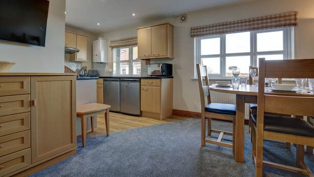Una cocina moderna con armarios de madera, lavavajillas integrado y un comedor con mesa y sillas.